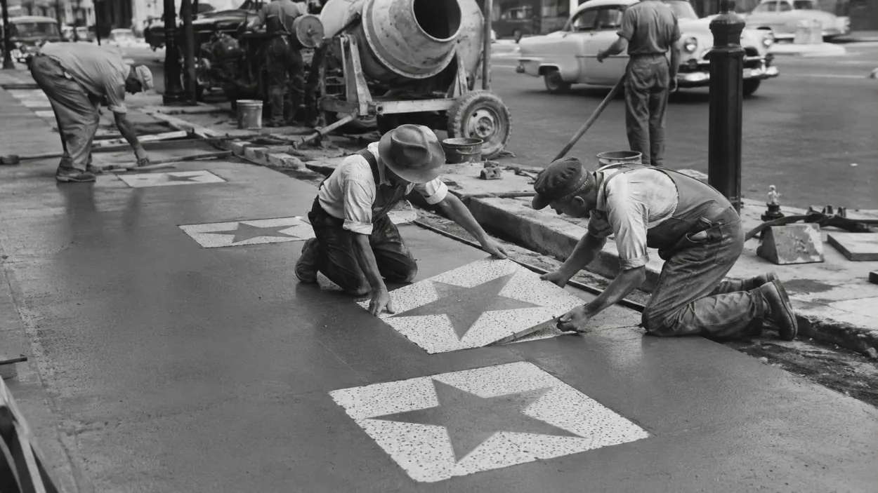 A vintage black-and-white scene of workers setting stars into a new sidewalk